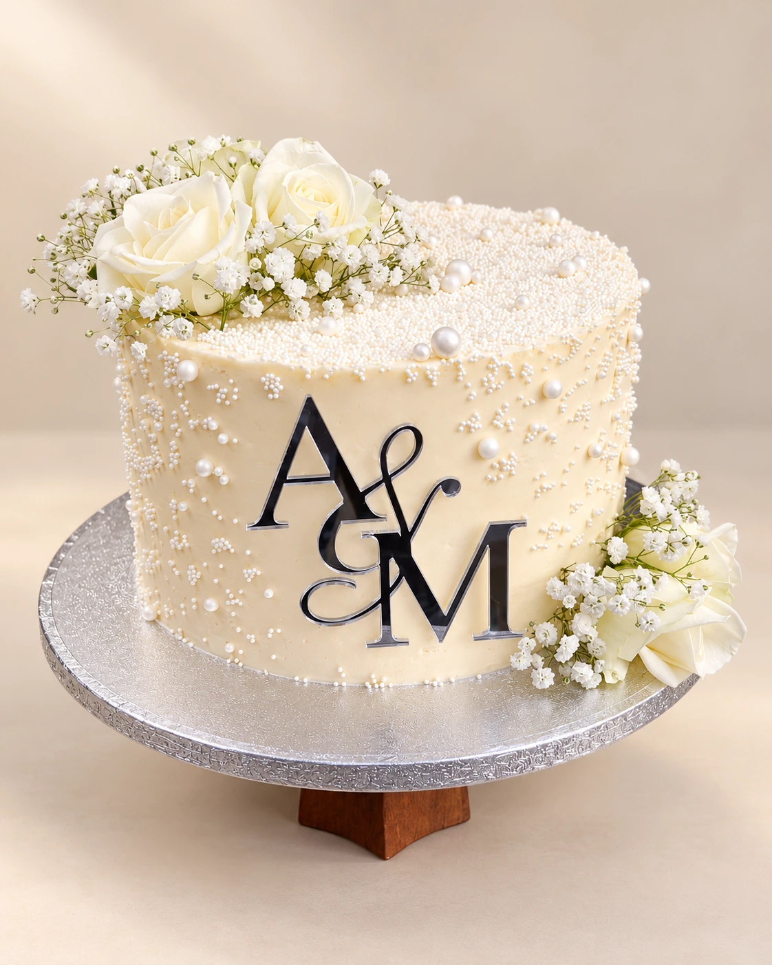 Ivory wedding cake with white roses, delicate white flowers, pearls and an A and M monogram